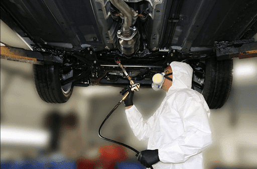 Technician spray-applying Vitacare rust protection to a vehicle underbody